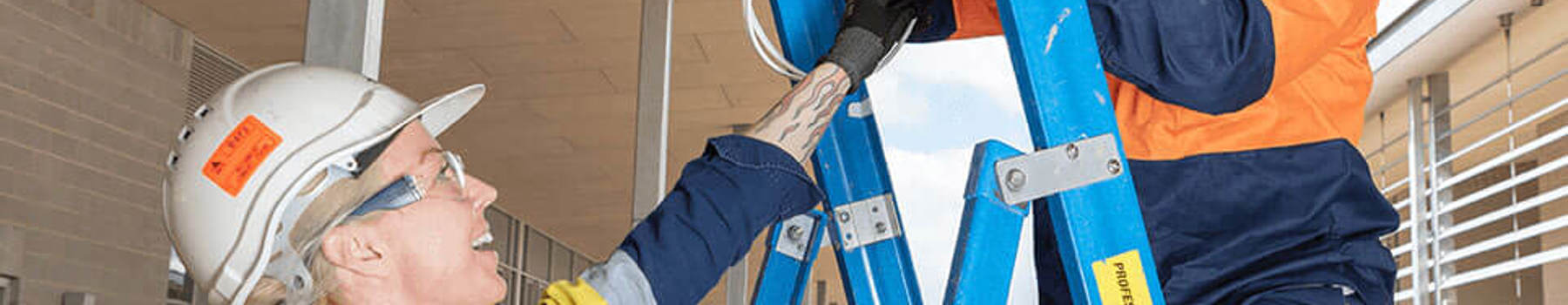 Female electrician working with a colleague on a ladder installing wiring